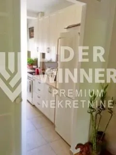 Pogled na manju kuhinju sa belim elementima i frižiderom.