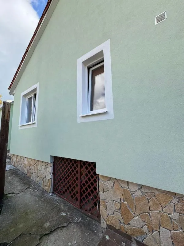 Bočna fasada kuće sa svijetlozelenom fasadom, kamenim podrumskim dijelom i prozorima.