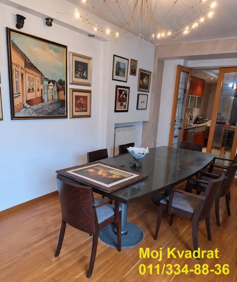 Trpezarija sa drvenim stolom, stolicama i slikama na zidu.