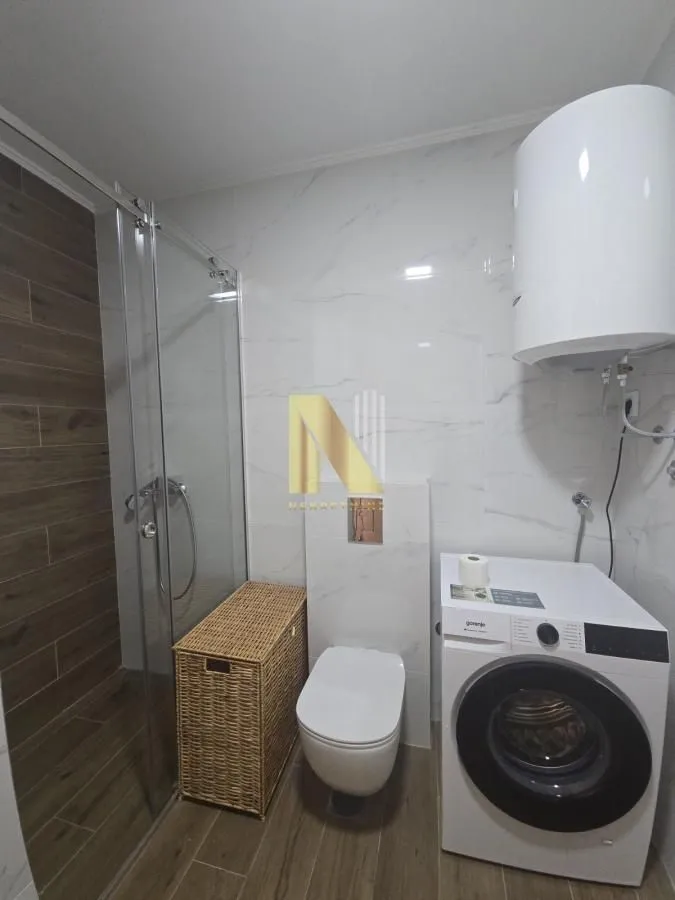 Moderno kupatilo sa tuš kabinom, WC šoljom i veš mašinom.
