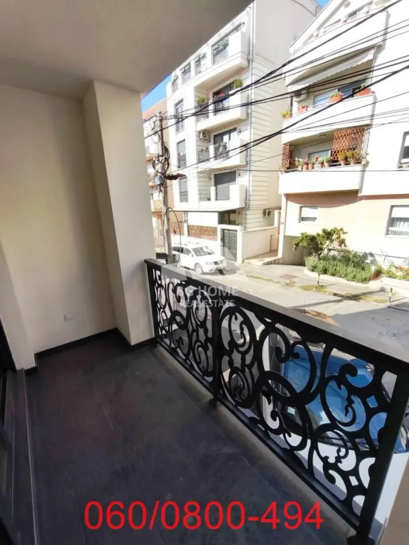 Natkriveni balkon sa ukrasnom metalnom ogradom i pogledom na ulicu i zgrade.
