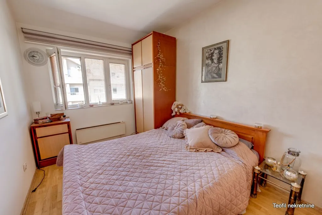Nameštena spavaća soba sa bračnim krevetom, garderoberom i prozorom.