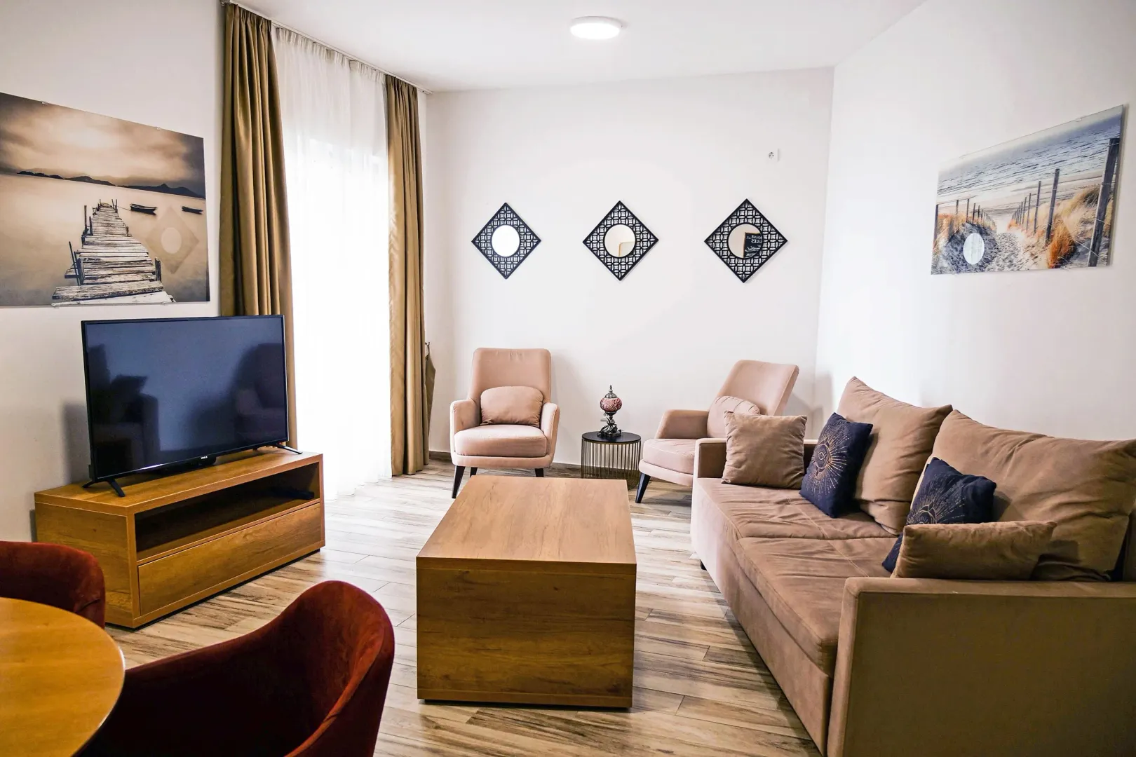 Dnevna soba sa garniturom, foteljama, TV-om i dekorativnim ogledalima na zidu.