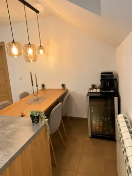 Trpezarija sa drvenim stolom, modernim osvetljenjem i aparatom za kafu u uglu. - image 5