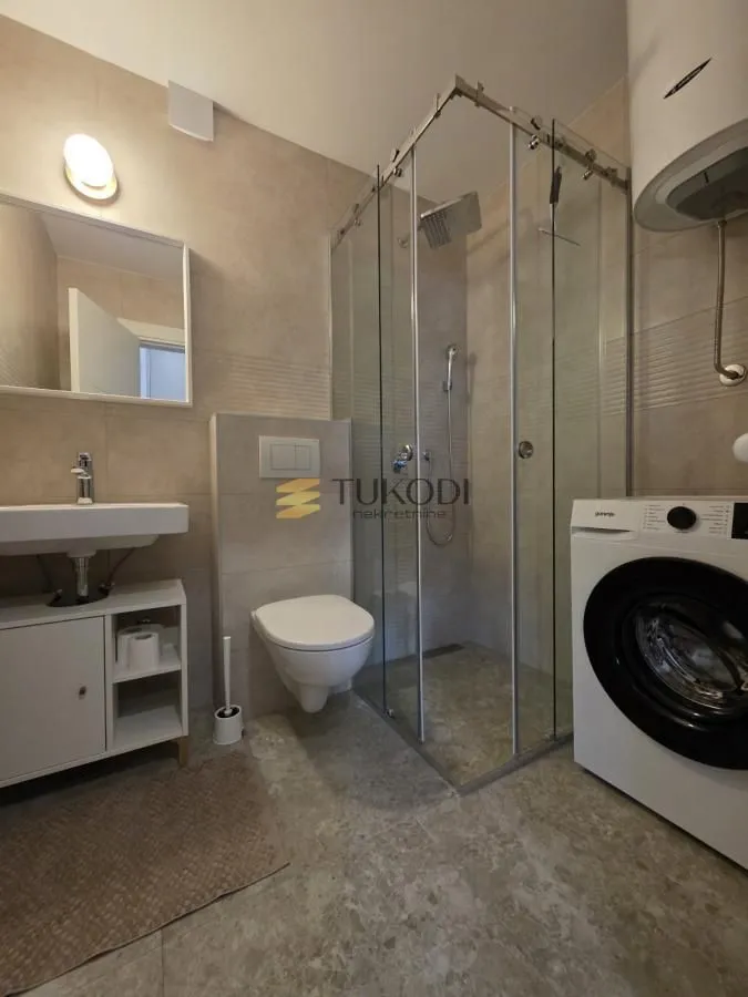 Moderno kupatilo sa tuš kabinom, umivaonikom i veš mašinom.