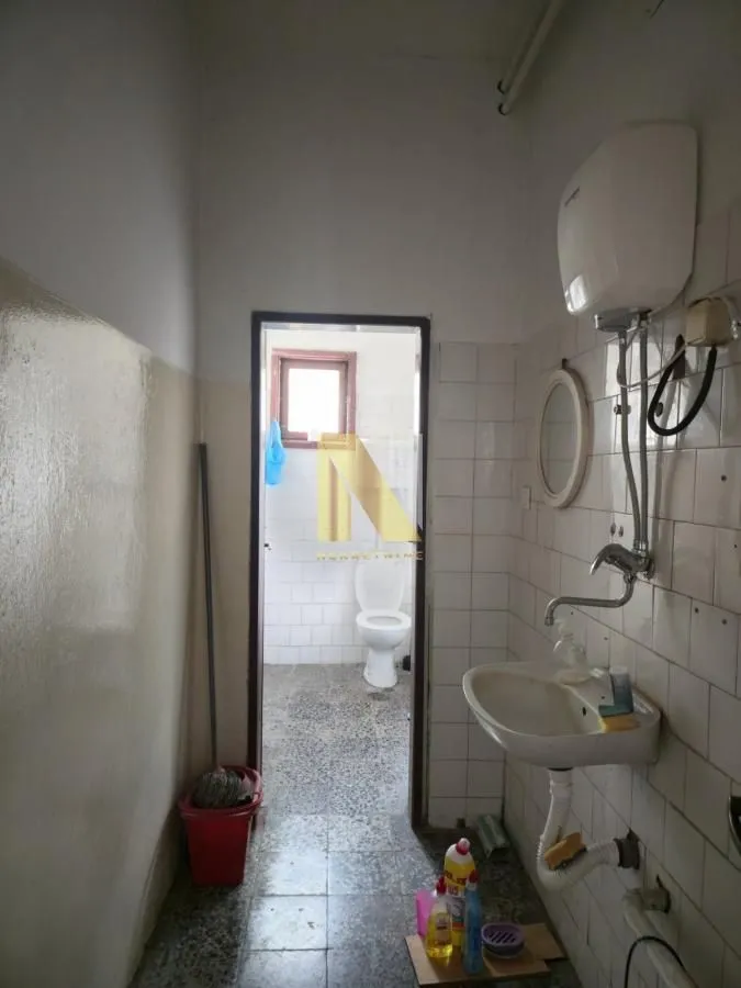Older bathroom with a sink and water heater, looking into an adjoining room with a toilet.