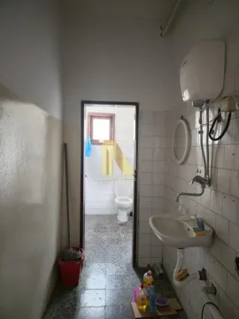 Older bathroom with a sink and water heater, looking into an adjoining room with a toilet. - image 5