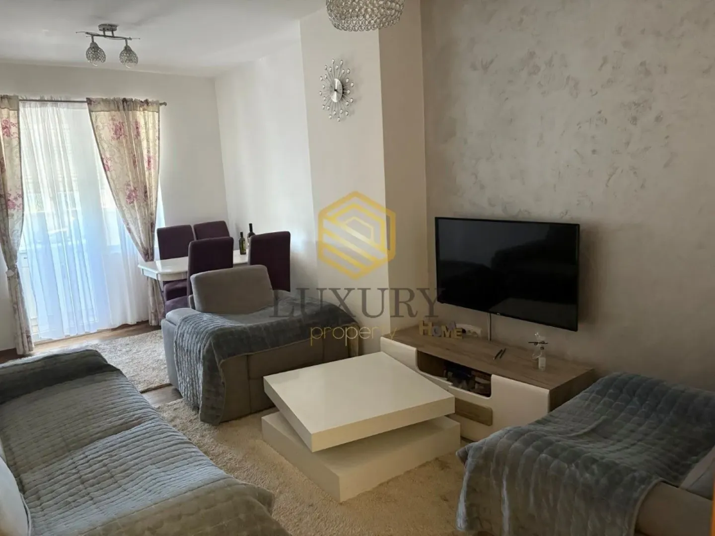 Living room with a sofa, TV, and dining area in the background.