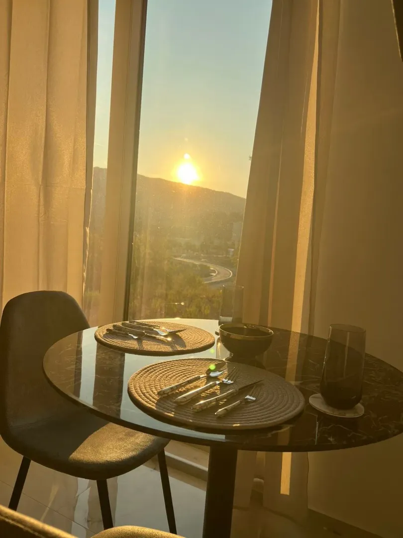 Dining table set for two by a large window with a sunset view.