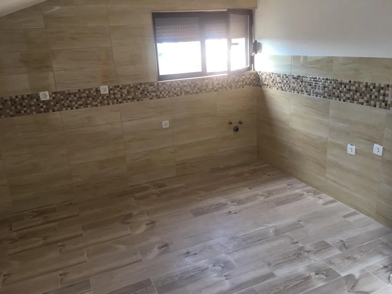 An empty room finished with ceramic tiles and a window.