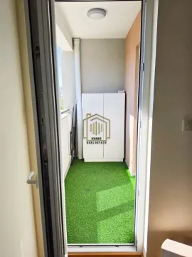 Pogled kroz vrata na uređeni balkon sa vještačkom travom i ormarićem. - image 11