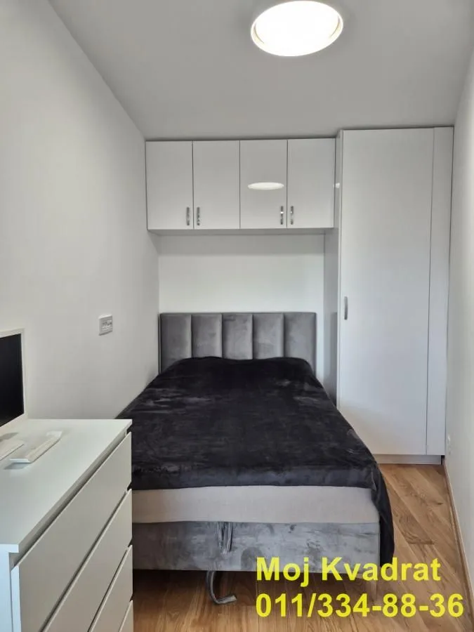 Manja spavaća soba sa krevetom, ugradnim ormanom i komodom.