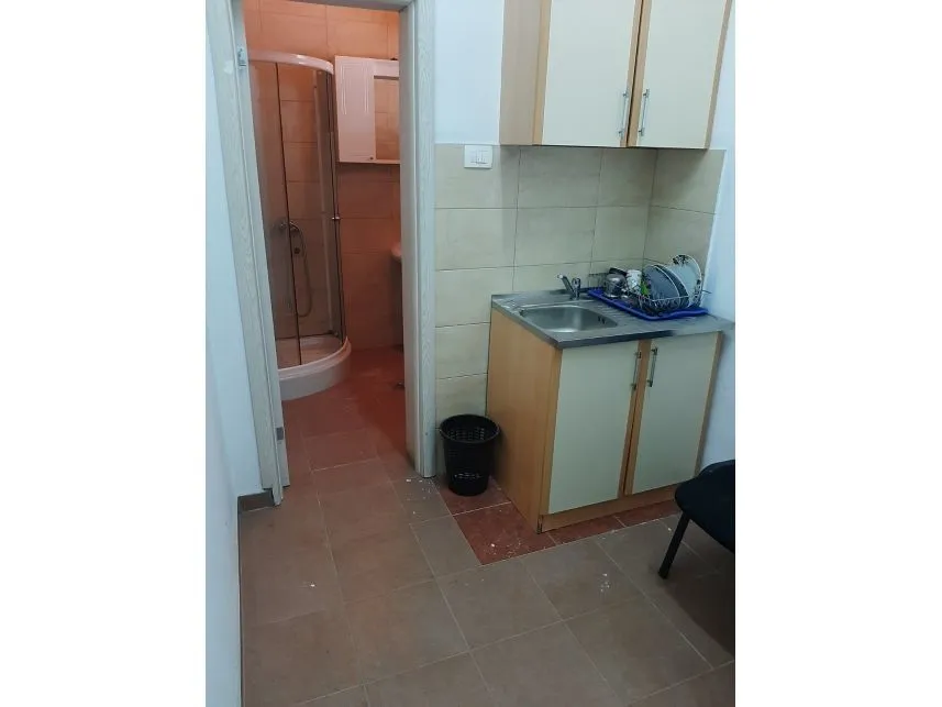 A small kitchen area with a sink next to the entrance of a bathroom with a shower.
