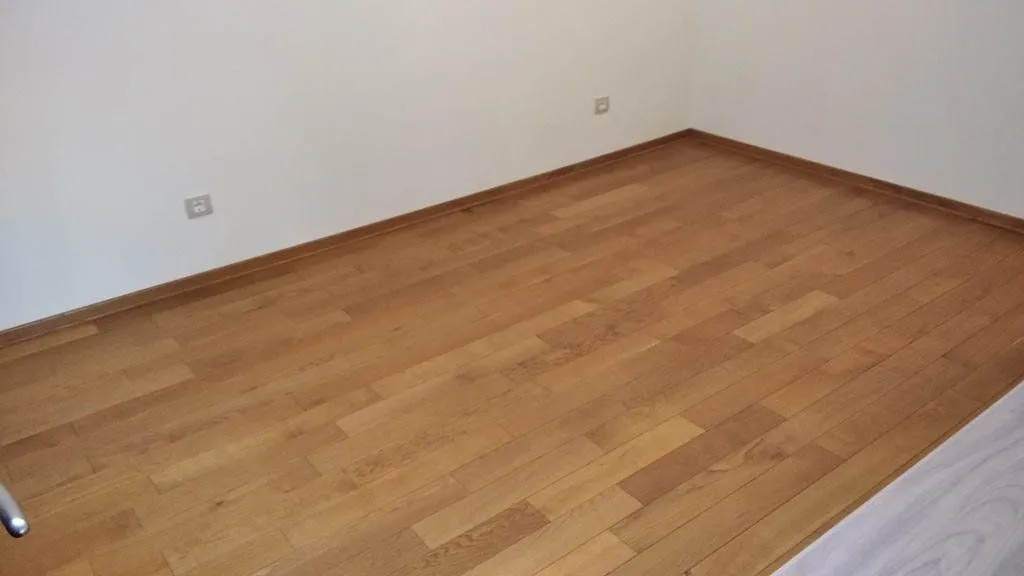 Prazna soba sa drvenim parketom i bijelim zidovima.