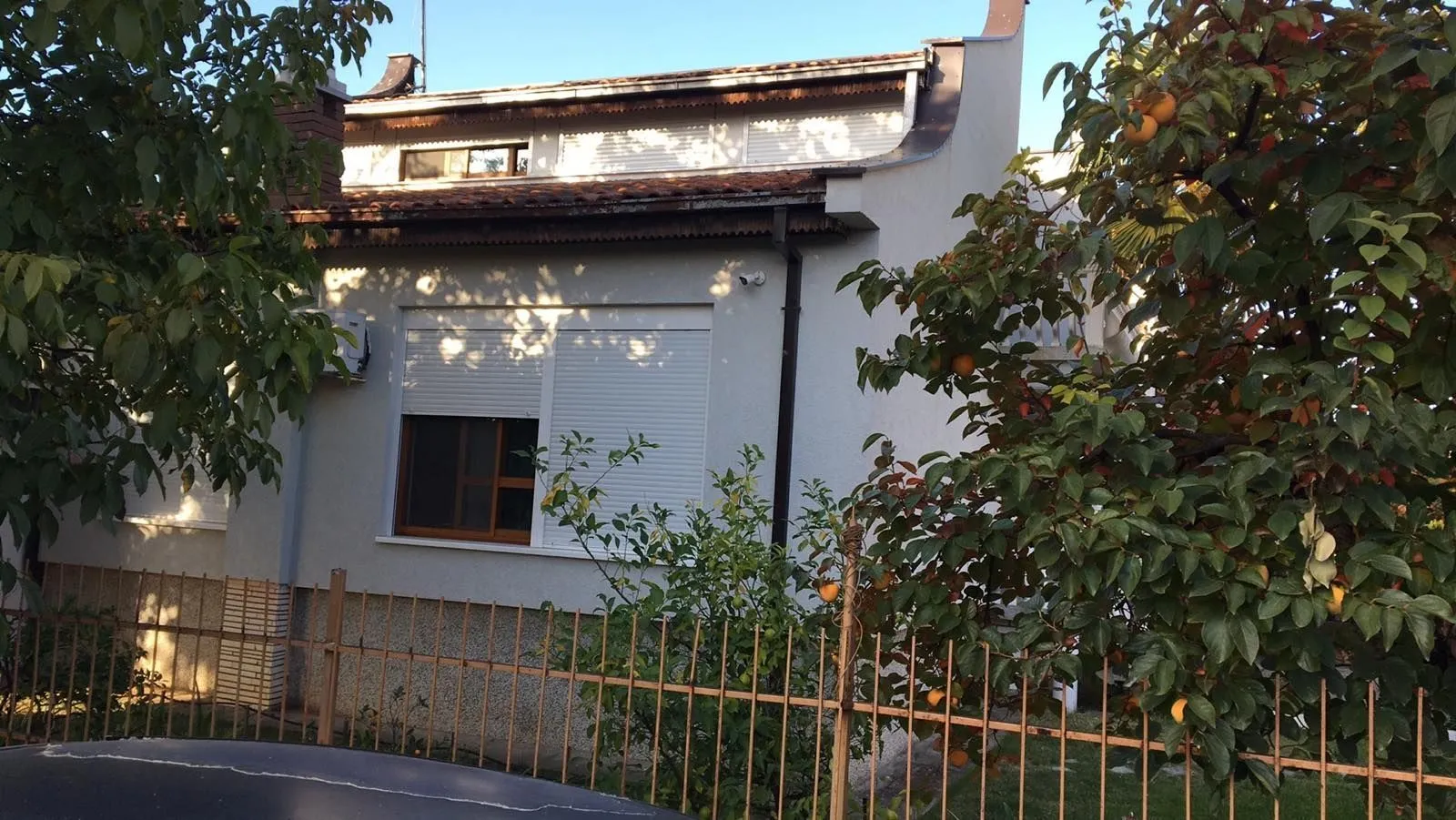 Exterior view of a two-story house with a fenced yard and fruit trees.