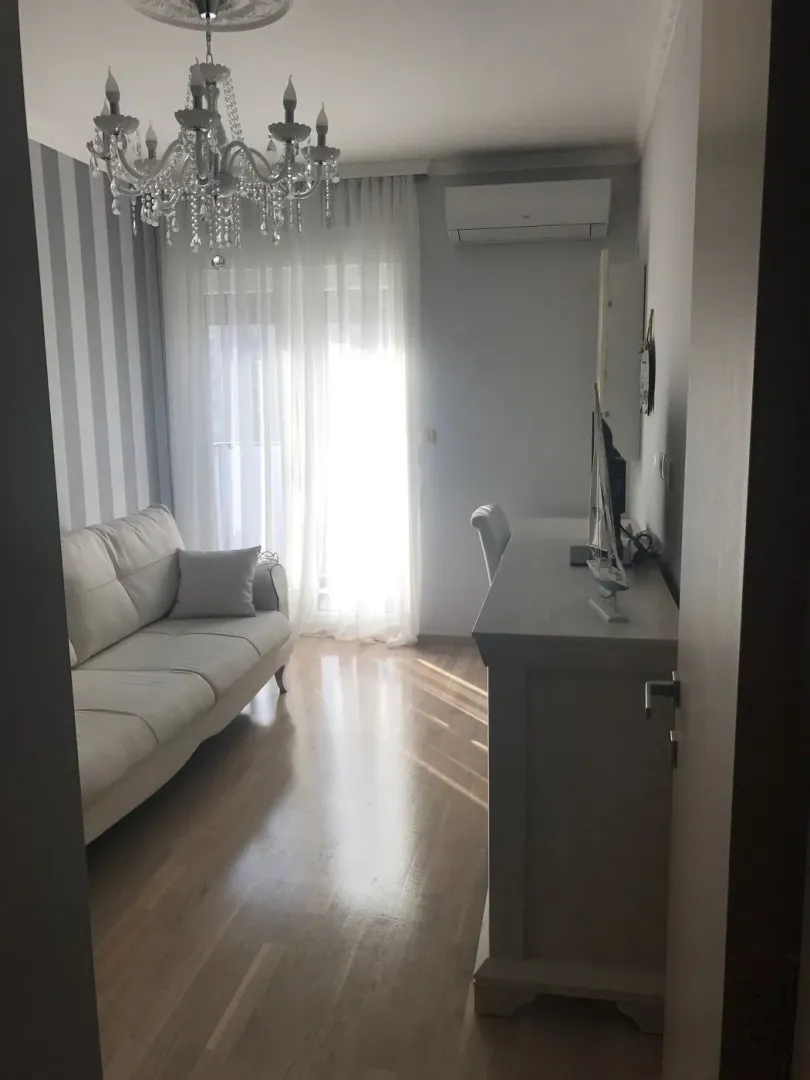 Svijetla dnevna soba sa bijelom garniturom i lusterom.