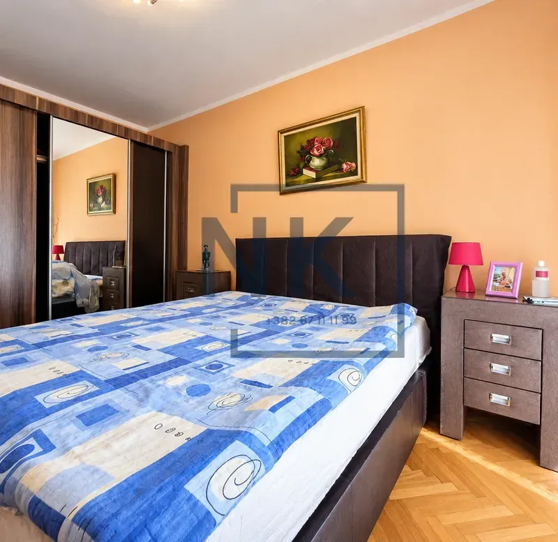 Namještena spavaća soba sa bračnim krevetom, plakarom sa ogledalom i noćnim stočićem.