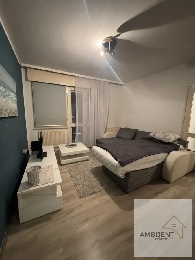 Dnevna soba sa garniturom, TV komodom i izlazom na terasu.