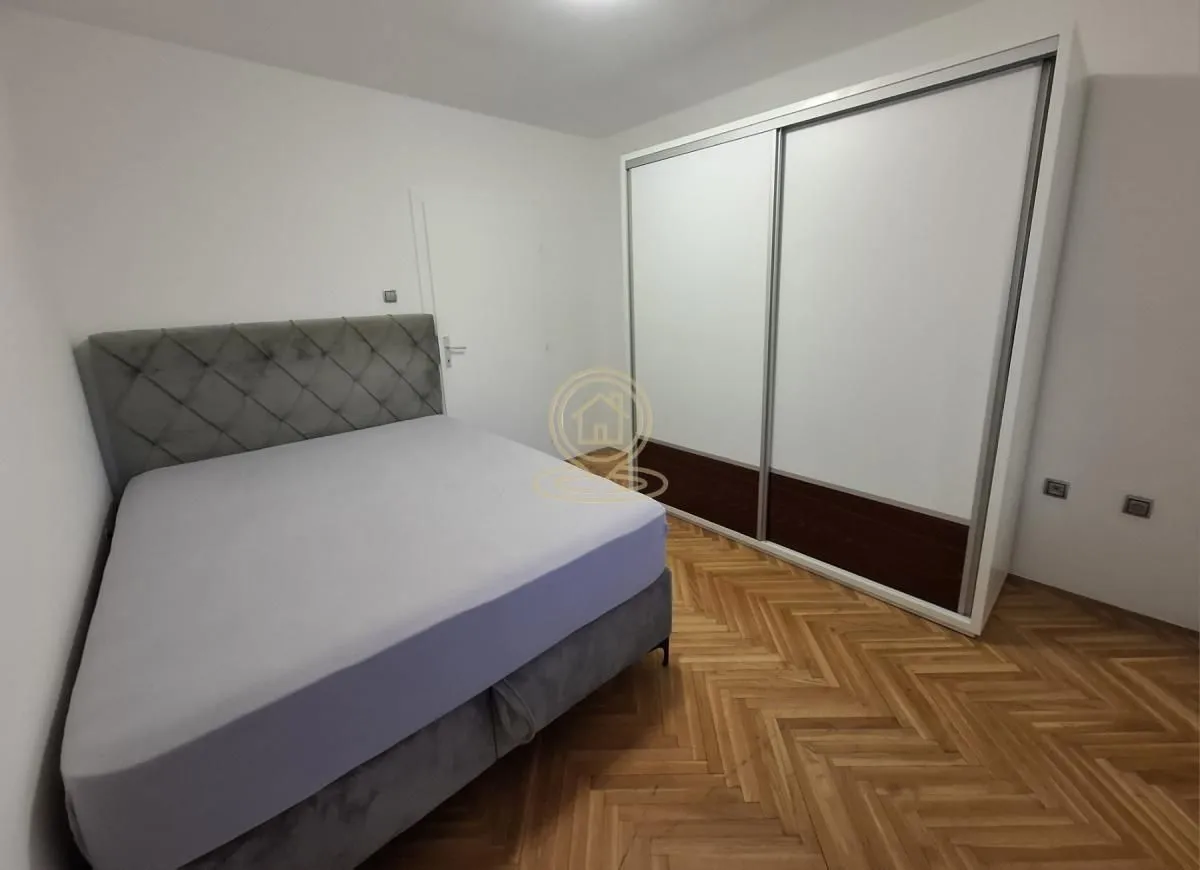 Spavaća soba sa bračnim krevetom, velikim garderoberom i parketom na podu.