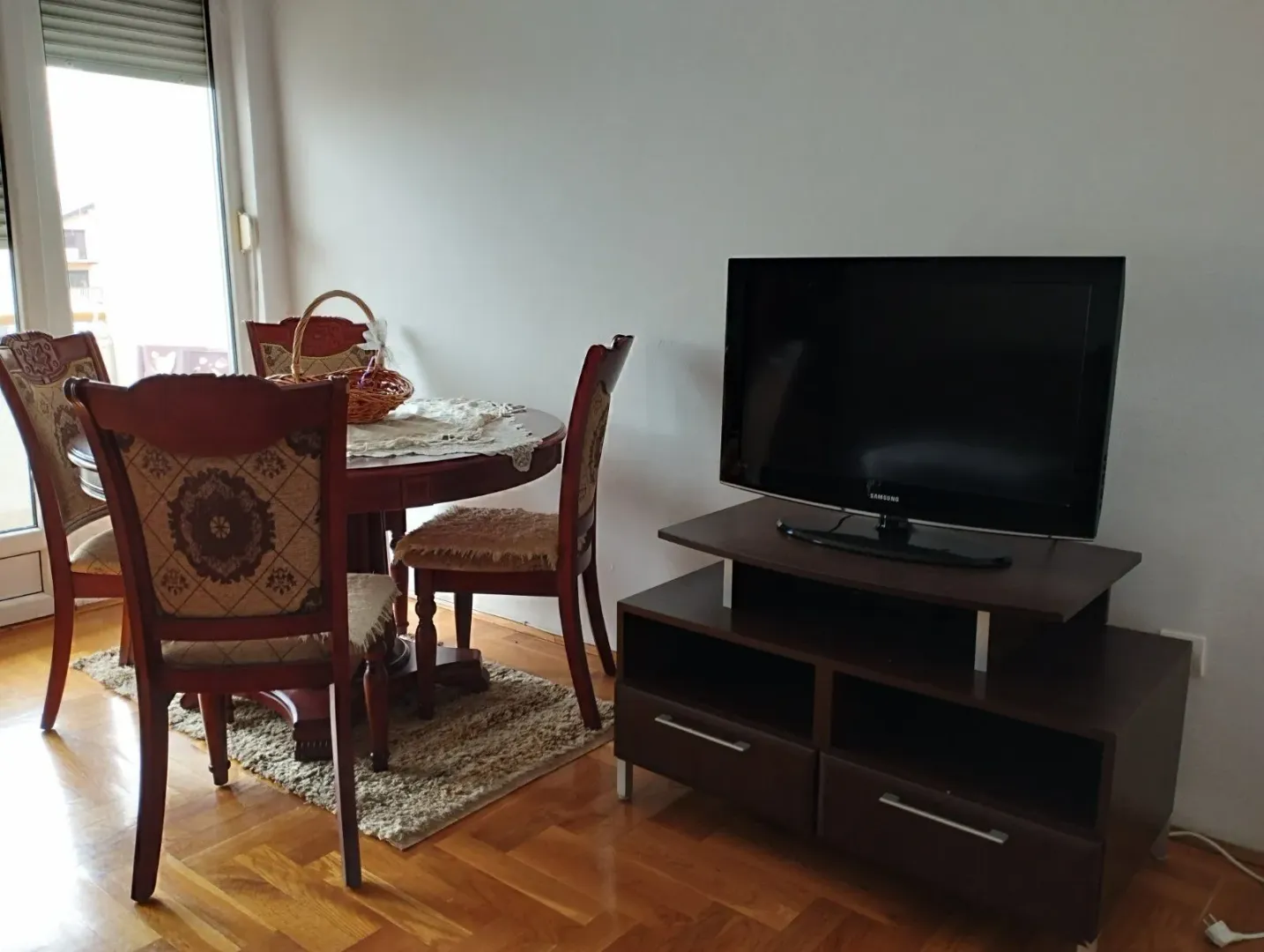 Trpezarijski sto sa stolicama i televizor na komodi u dnevnoj sobi.