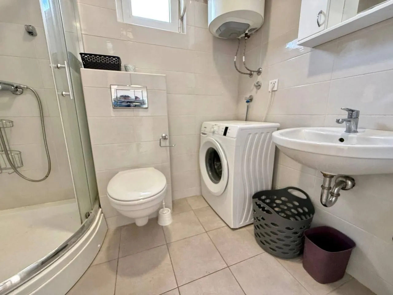 Compactly equipped bathroom with a shower cabin, sink, and washing machine.