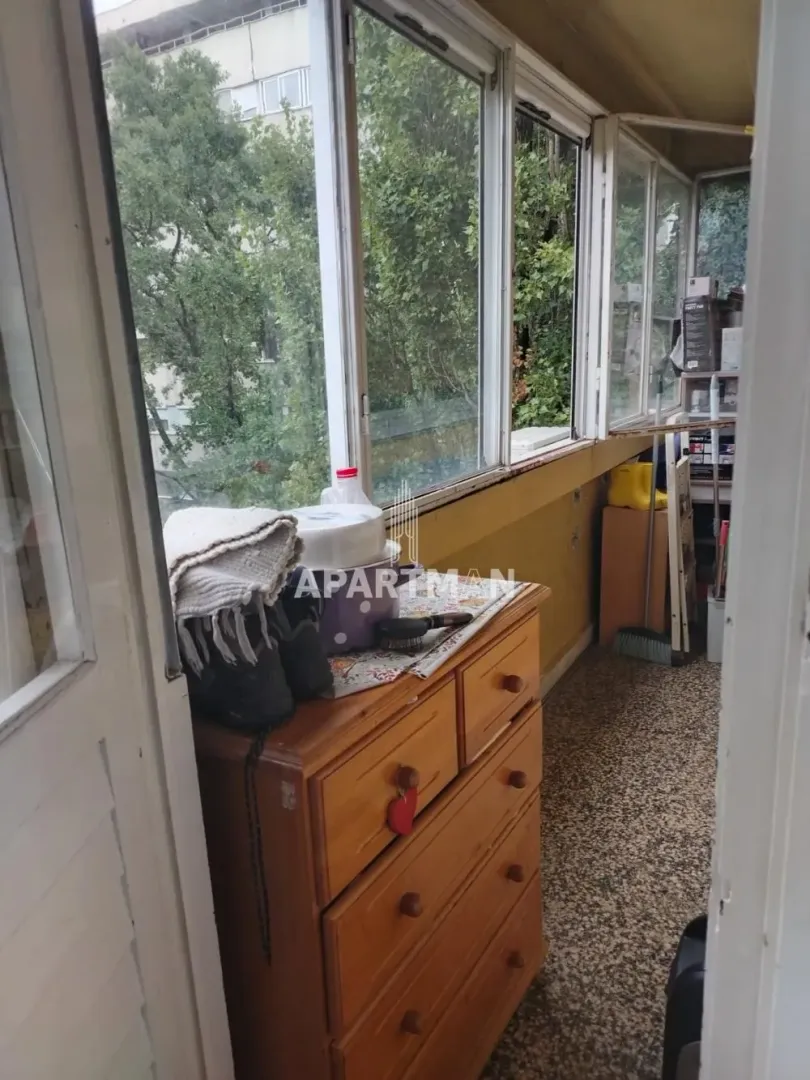 Zastakljena terasa sa komodom i pogledom na zelenilo.