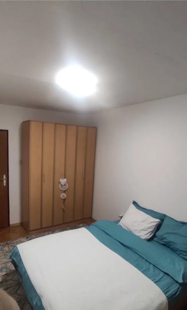 Jednostavno namještena spavaća soba sa drvenim ormarom i bračnim krevetom.