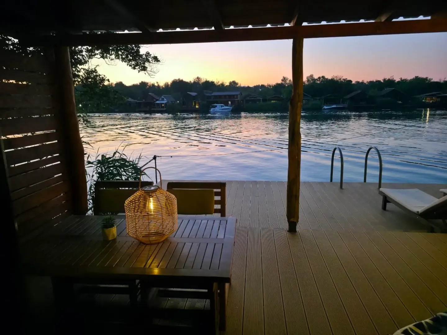 Drvena terasa sa stolom i pogledom na rijeku u sumrak.