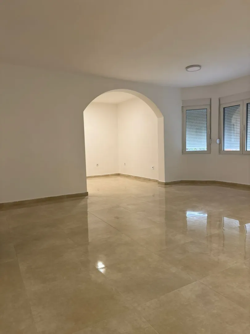 Spacious and bright empty room with tiled flooring and an arched doorway.