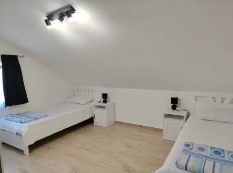 Potkrovna spavaća soba sa dva kreveta i bijelim namještajem. - image 9