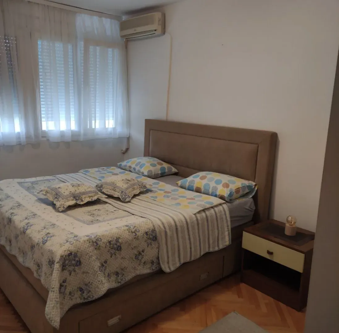 Namještena spavaća soba sa bračnim krevetom, noćnim stočićem i klima uređajem.