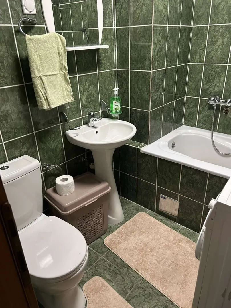 Kupatilo sa zelenim pločicama, kadom i umivaonikom.