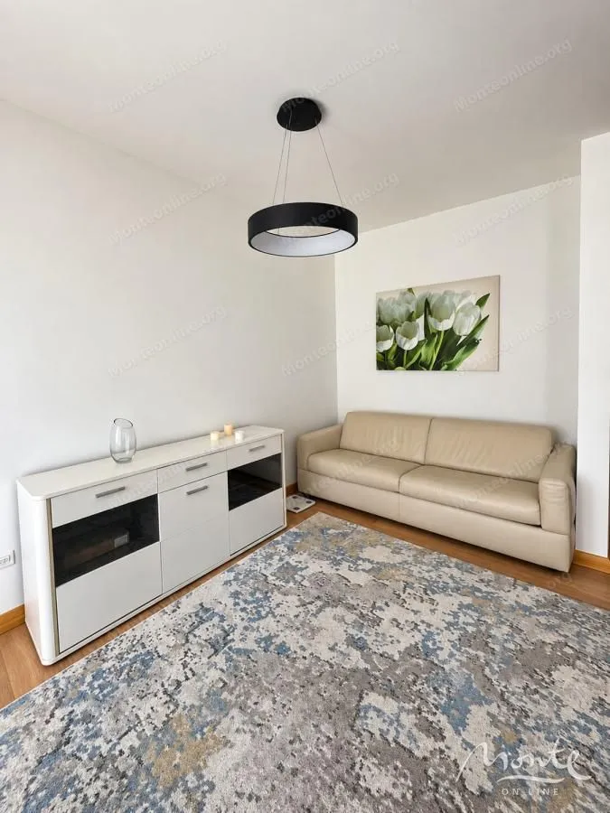 Dnevna soba sa bež kaučem, bijelom komodom i modernim lusterom.