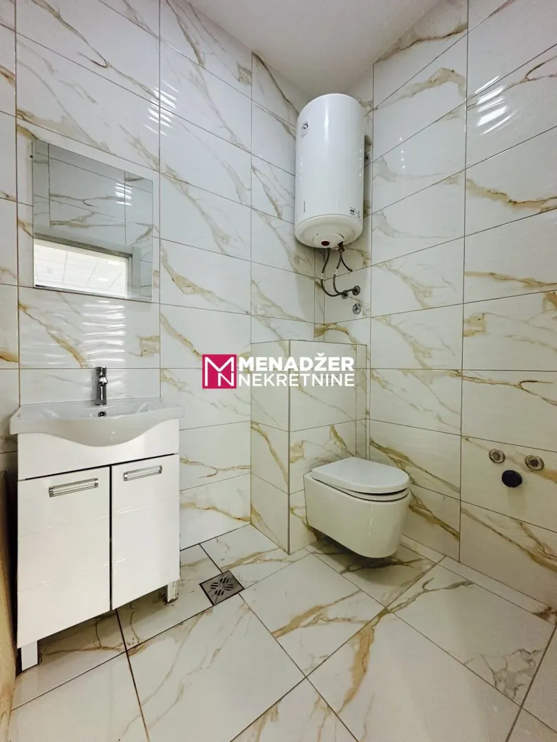 Small bathroom lined with marble tiles, featuring a sink and a toilet.