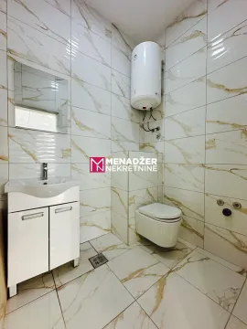 Small bathroom lined with marble tiles, featuring a sink and a toilet. - image 4