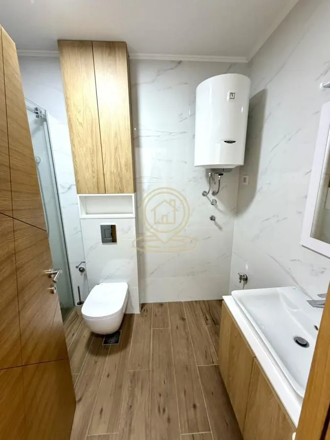 Modern bathroom with a shower cabin, toilet, sink, and water heater.