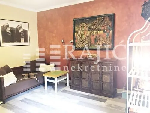 Living room furnished with a sofa, coffee table, chest of drawers, and artworks on the wall.