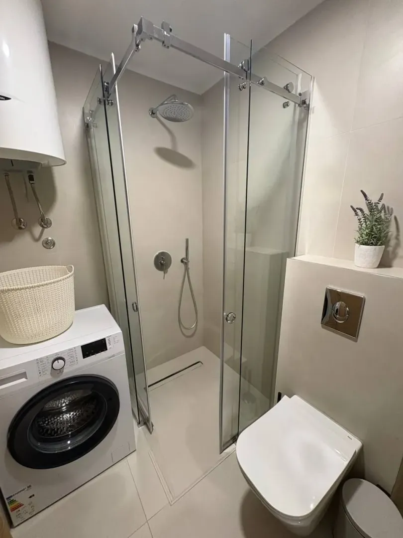 Moderne kupatilo sa tuš kabinom, wc šoljom i veš mašinom.