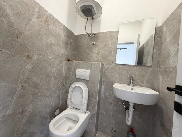 Small tiled bathroom with a toilet, washbasin, and water heater.