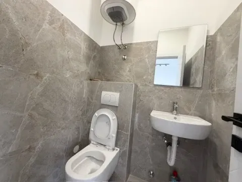 Small tiled bathroom with a toilet, washbasin, and water heater. - image 2