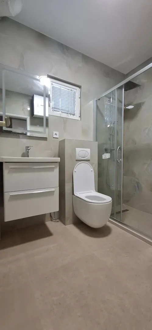 Moderne kupatilo sa tuš kabinom, konzolnom šoljom i umivaonikom.