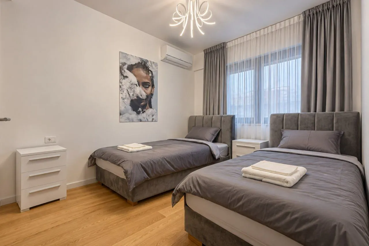 Modern bedroom with two single beds, parquet flooring, and a large window.