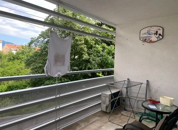 Covered balcony with a drying rack, a small table, and green views.