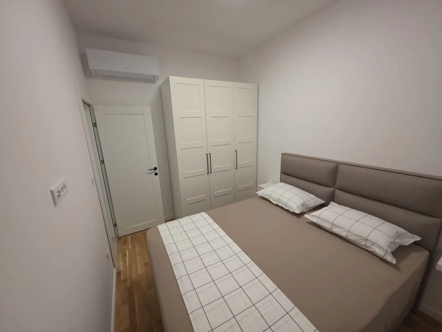 Furnished bedroom with a double bed, white wardrobe, and air conditioning.