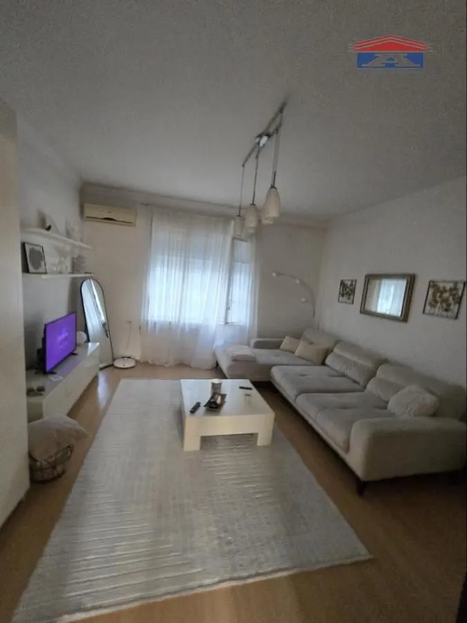 Dnevna soba sa ugaonom garniturom, stočićem i televizorom.