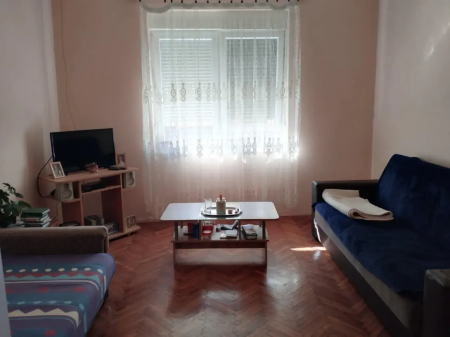 Dnevna soba sa garniturom, TV komodom i prozorom sa zavesama.