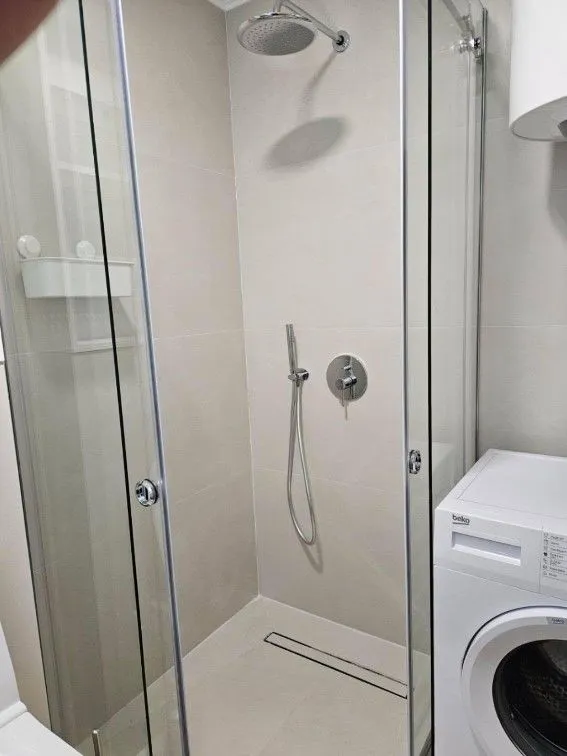 Moderno opremljeno kupatilo sa tuš kabinom i veš mašinom.