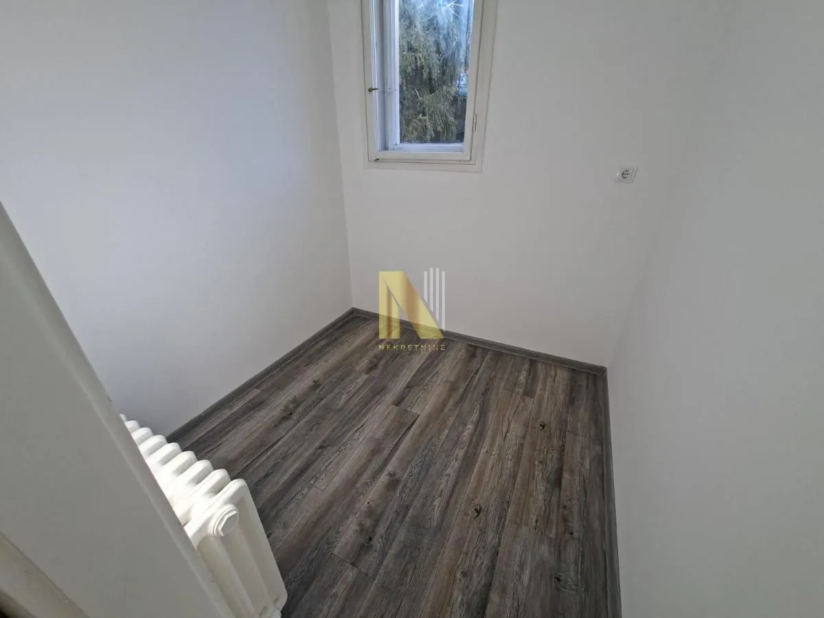 Manja prazna prostorija sa tamnim laminatom i prozorom.