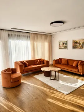 Living room furnished with orange sofas, a wooden coffee table, and paintings on the wall. - image 6