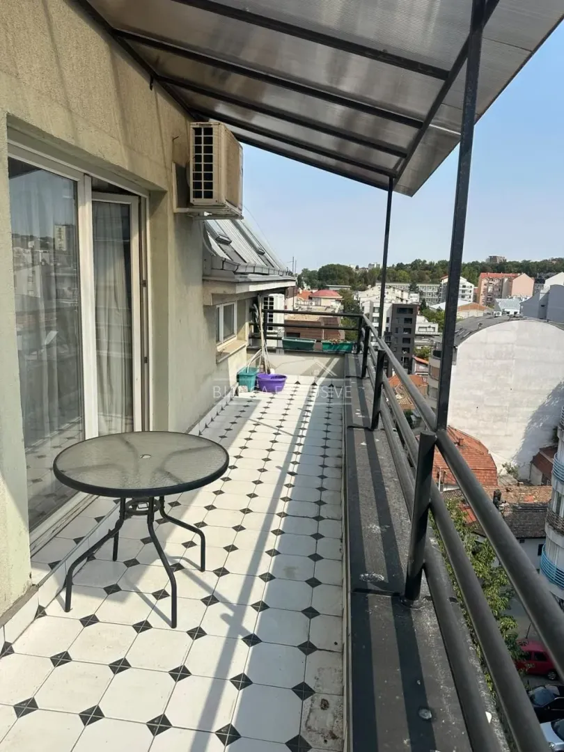 Dugi natkriveni balkon sa stolom i pogledom na grad.